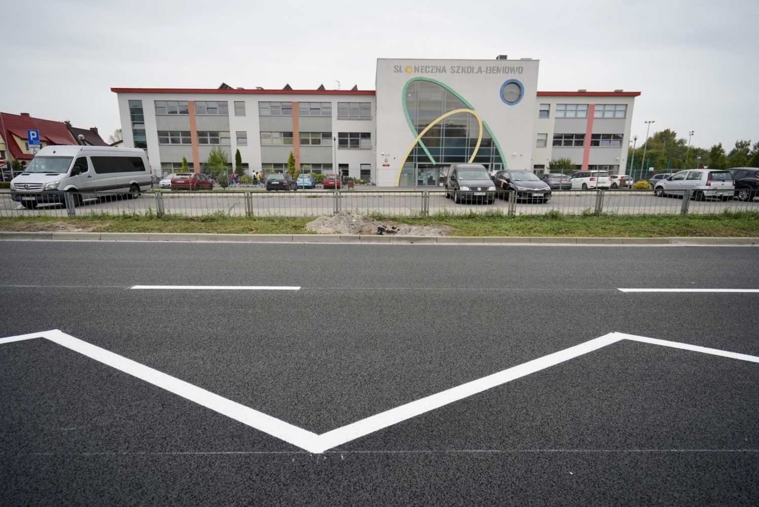 Słoneczna Szkoła w Jędrzejowie. Nowoczesny budynek szkoły z zaparkowanymi przed nim samochodami.