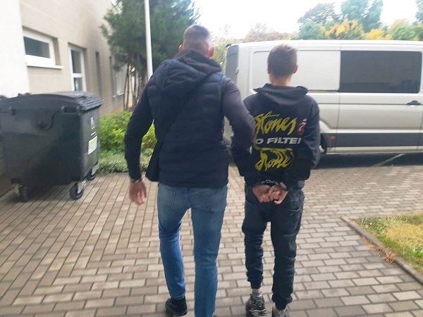 Policjant eskortujący skutego kajdankami nieletniego.