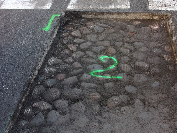 Naprawa drogi ukazująca odsłonięte kostki brukowe oznaczone zieloną literą „2”.