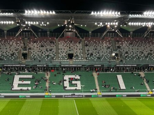 Częściowo wypełniony stadion z napisem „E-G-I” na siedzeniach podczas meczu Ligi Konferencji Europejskiej UEFA.