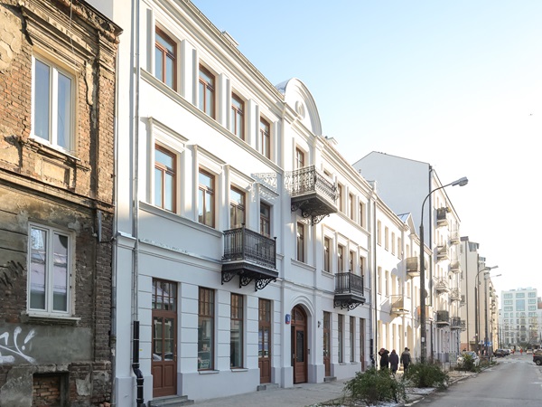 Odnowione białe budynki z balkonami stoją wzdłuż miejskiej ulicy.