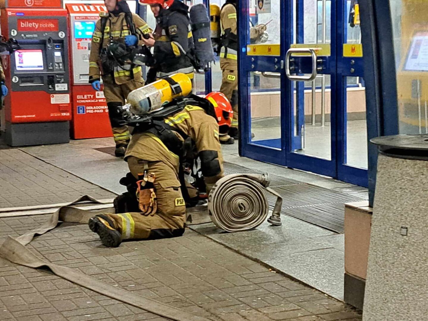 Strażacy biorący udział w akcji gaśniczej w pobliżu automatu biletowego.