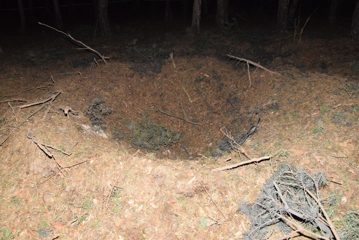 Krater w lesie sosnowym nocą, prawdopodobnie powstały w wyniku wybuchu bomby lub innej eksplozji.