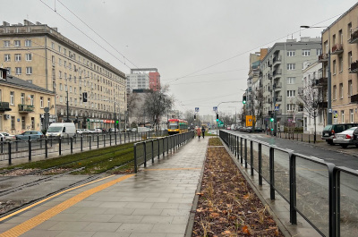Widok na tory tramwajowe i chodnik dla pieszych w Warszawie w deszczowy dzień.