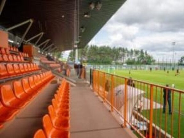 Puste pomarańczowe siedzenia stadionu z widokiem na boisko do piłki nożnej.