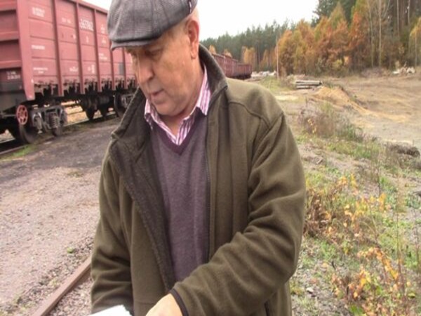 Mężczyzna w czapce przeglądający dokumenty w pobliżu wagonów kolejowych