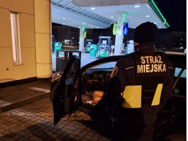 Funkcjonariusz Straży Miejskiej pomagający nocą na stacji benzynowej.