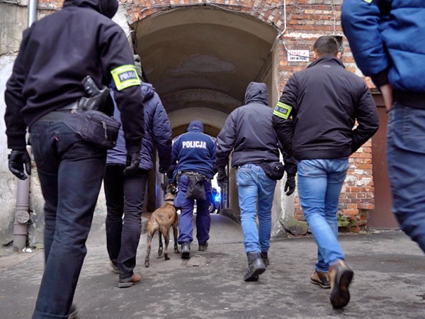 Policjanci i jednostka K-9 badają miejsce zbrodni w zaułku.