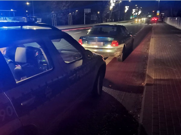 Samochód policyjny zatrzymuje pojazd w nocy podczas kontroli drogowej.