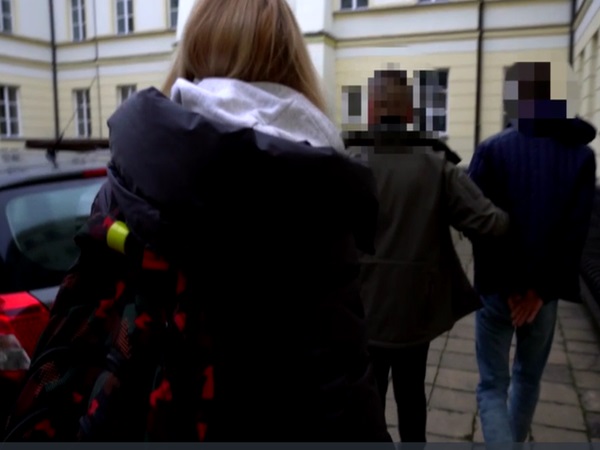 Widok z tyłu młodej kobiety i dwóch mężczyzn eskortowanych przez policję.