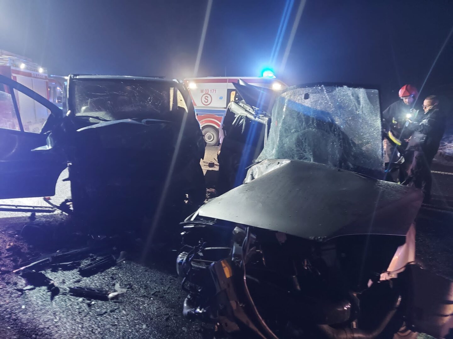 Poważnie uszkodzone pojazdy po wypadku samochodowym w nocy. Na miejscu są służby ratunkowe.