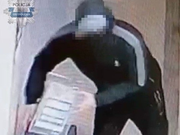 Obraz z monitoringu ukazujący zakapturzonego podejrzanego niosącego paczkę.
