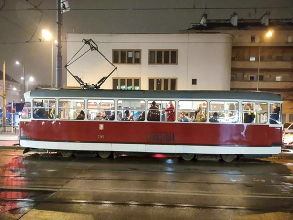 Czerwono-biały zabytkowy tramwaj nr 795, pełen pasażerów w deszczową noc.