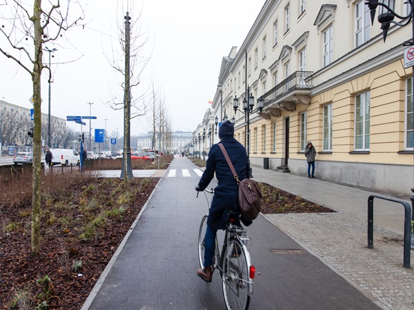 Osoba jadąca na rowerze po miejskiej ścieżce rowerowej w pobliżu eleganckich budynków.