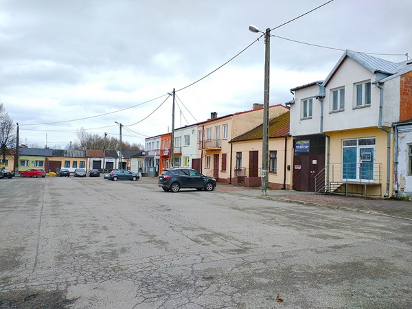 Pusty rynek miejski z zaparkowanymi samochodami i pastelowymi budynkami.