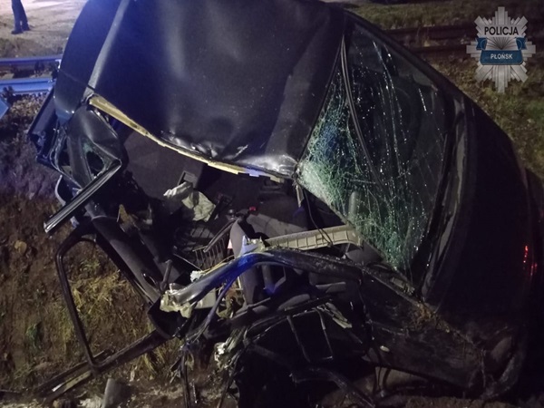 Samochód poważnie uszkodzony po kolizji, widoczne poważne uszkodzenia dachu i przedniej szyby.