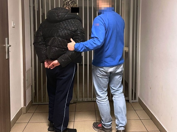 Policjant eskortujący skutego podejrzanego przez zabezpieczony obszar.