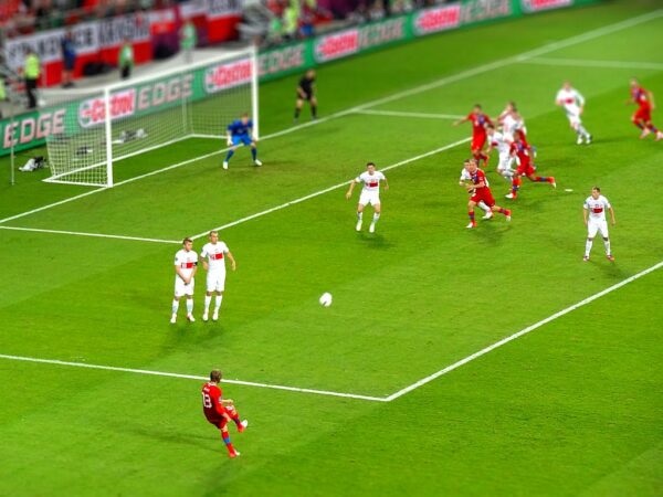 Piłkarz kopie piłkę podczas rzutu wolnego. Inni gracze obserwują.