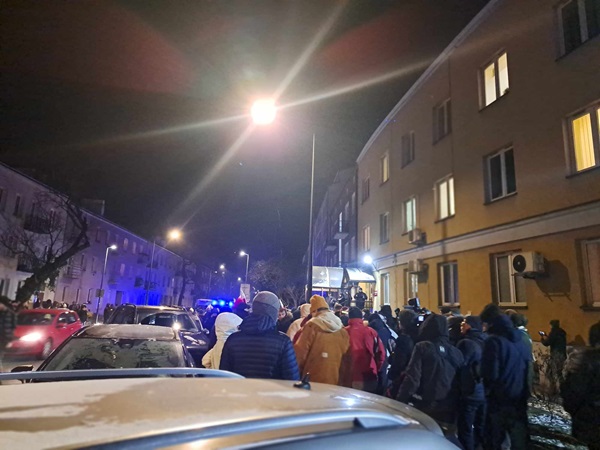 Nocny protest: tłum zbiera się na ulicy miasta, w pobliżu zaparkowane są samochody.