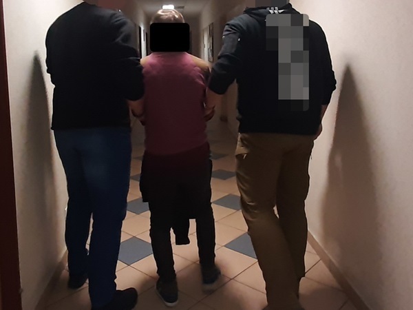 Dwóch funkcjonariuszy eskortuje osobę korytarzem.