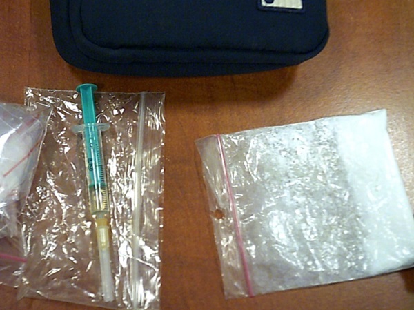 Zbliżenie strzykawki, woreczków z białym proszkiem i małego, czarnego woreczka.