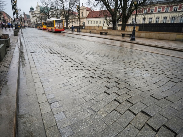 Mokra, brukowana ulica w europejskim mieście. W oddali widać autobusy.