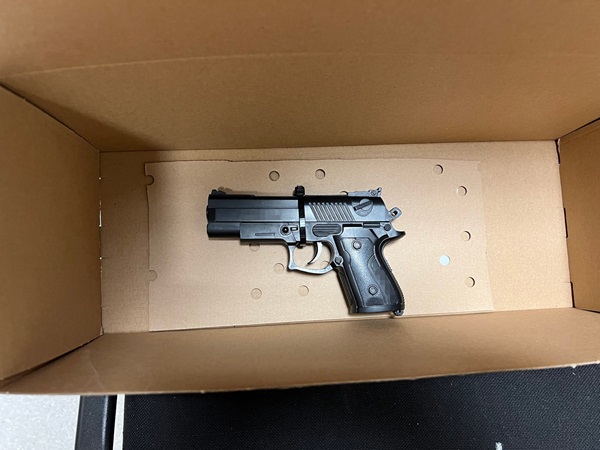 Czarny pistolet w tekturowym pudełku z ochronnymi wkładkami piankowymi.