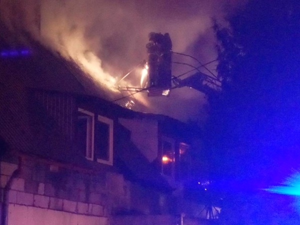Strażacy gaszą pożar domu w nocy, korzystając z wozu drabinowego.