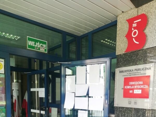 Wejście do Biblioteki Publicznej z tablicą komisji wyborczej „Obwodowa Komisja Wyborcza”.