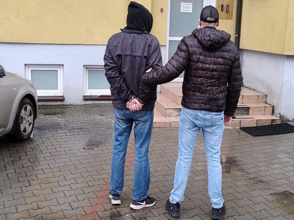 Policjant aresztujący podejrzanego przed budynkiem.