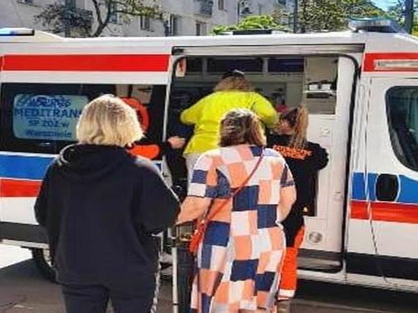 Ludzie stoją w pobliżu karetki pogotowia, niektórzy wydają się otrzymywać pomoc medyczną.