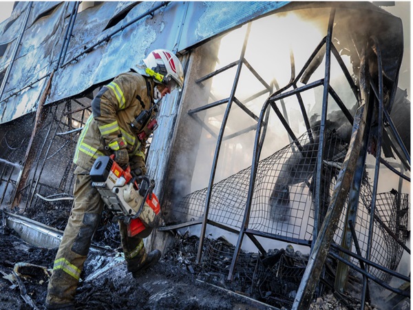 Strażak używa piły łańcuchowej do przecinania gruzów na miejscu pożaru.