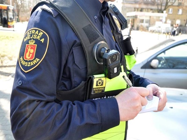 Funkcjonariusz Straży Miejskiej w Warszawie wypisuje mandat, mając na sobie kamerę