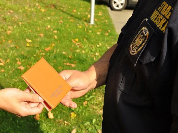 Zbliżenie ręki wręczającej polską legitymację funkcjonariuszowi Straży Miejskiej.