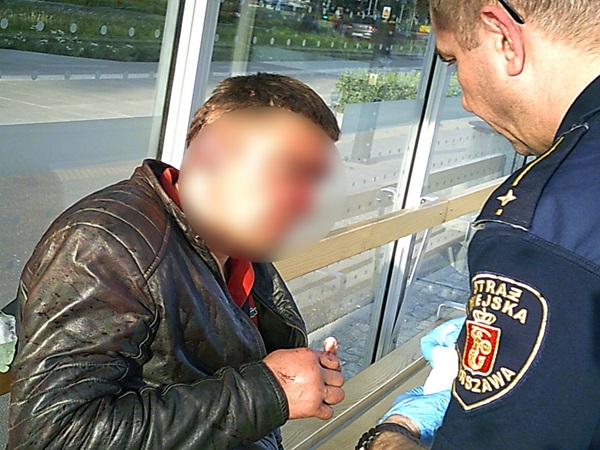 Ranny mężczyzna otrzymuje pierwszą pomoc od polskiego policjanta na przystanku autobusowym.