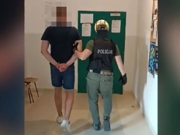 Policjant eskortujący skutego kajdankami podejrzanego korytarzem.