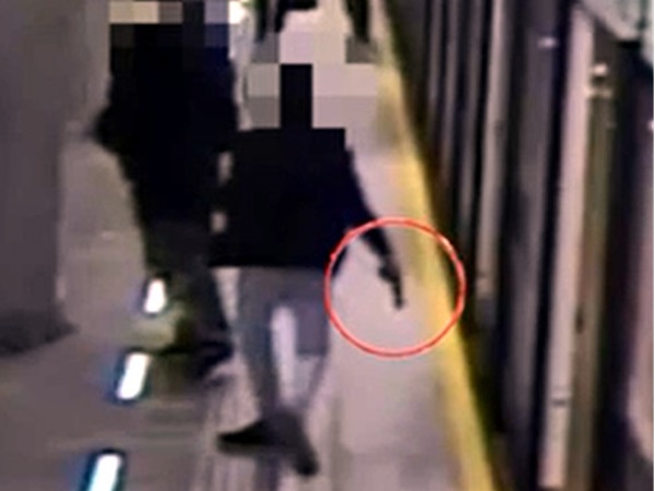 Rozmazany obraz z monitoringu przedstawiający osobę trzymającą broń na peronie metra.