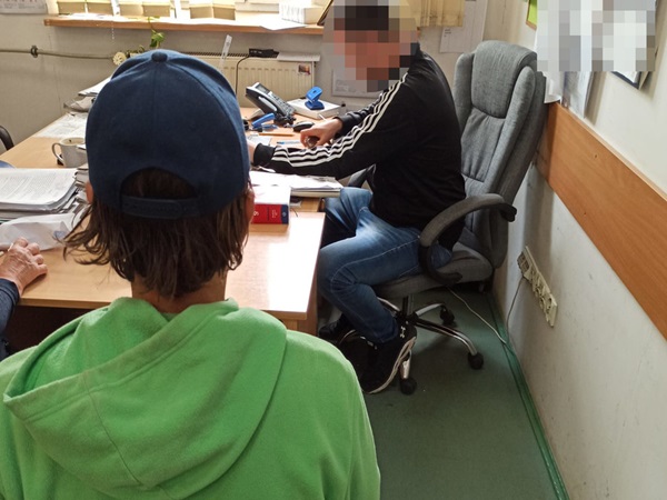 Dwie osoby siedzą przy stole w biurze, jedna ma na sobie zieloną bluzę z kapturem, druga dżinsy.