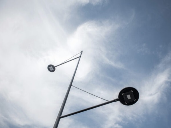 Nowoczesna latarnia uliczna z dwiema lampami LED na tle zachmurzonego nieba.