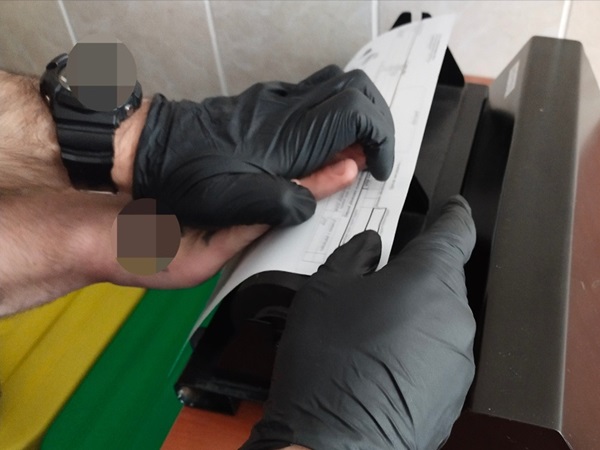 Osoba korzystająca ze skanera linii papilarnych w czarnych rękawiczkach.