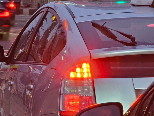 Widok z tyłu srebrnej Toyoty Prius w ruchu ulicznym, z włączonymi światłami hamowania.