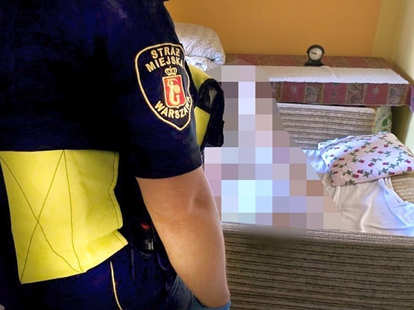 Funkcjonariusz Straży Miejskiej w Warszawie pomaga osobie leżącej na kanapie.