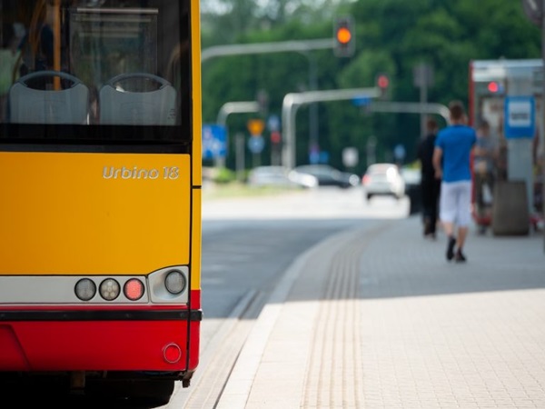 Widok z tyłu żółtego i czerwonego autobusu Urbino 18 na przystanku autobusowym