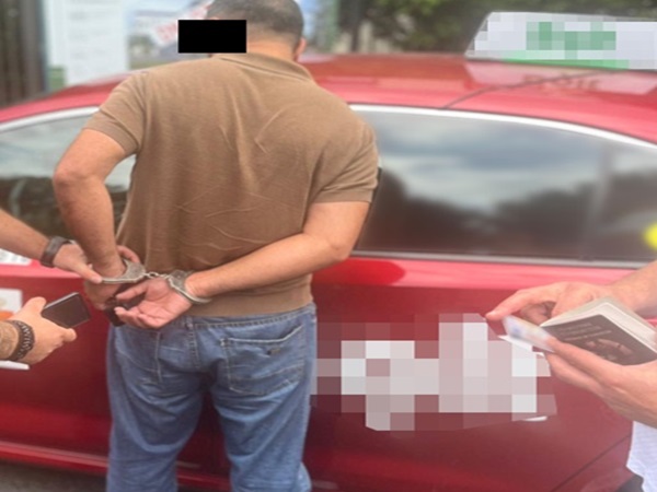 Mężczyzna w kajdankach aresztowany przez policję w pobliżu czerwonego samochodu.