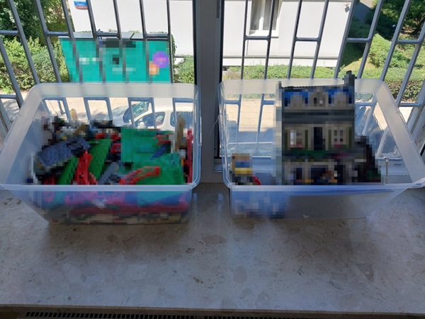 Dwa pojemniki z klockami LEGO, jeden z różnymi elementami, drugi zawierający duży budynek LEGO.