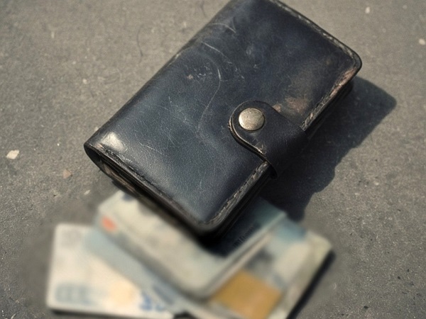 Zużyty skórzany portfel z pieniędzmi wysypującymi się na szarą powierzchnię