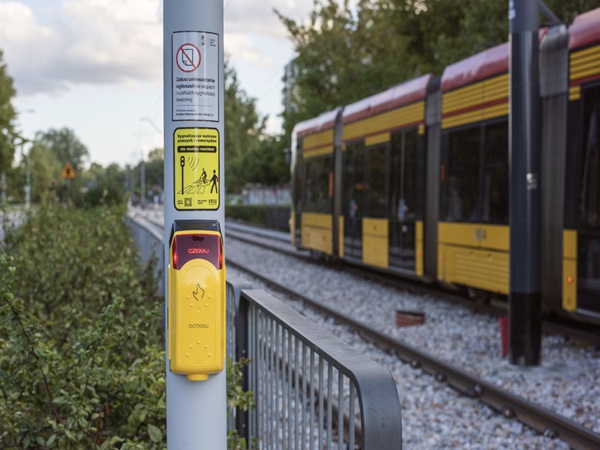Żółty przycisk przejścia dla pieszych na słupku przy tramwaju