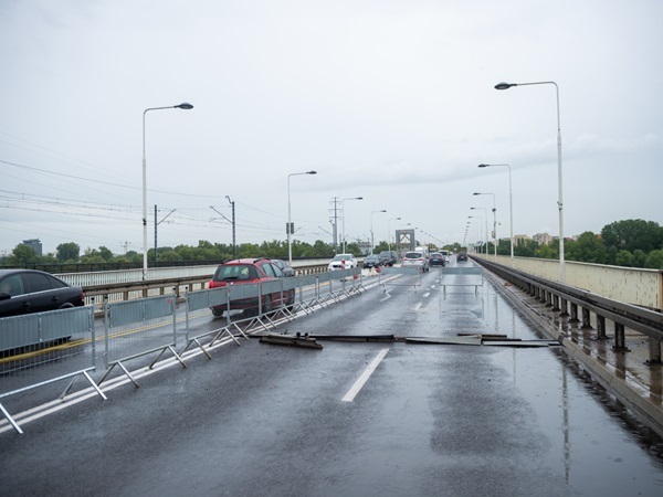 Uszkodzona jezdnia mostu z tymczasowymi barierami i mokrą nawierzchnią.