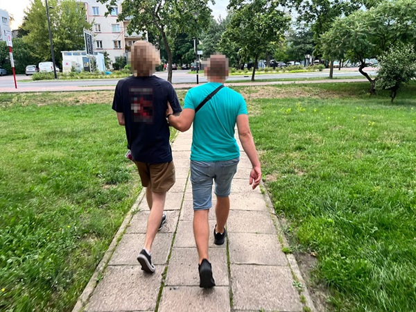 Dwóch młodych mężczyzn idzie chodnikiem, jeden prowadzi drugiego.