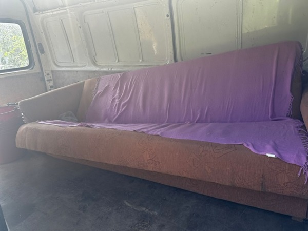 Brązowa sofa rozkładana w furgonetce, przykryta fioletowym kocem.
